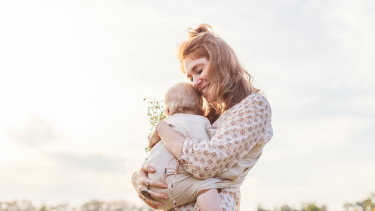 mom holding baby with flower in hand on first mother's day