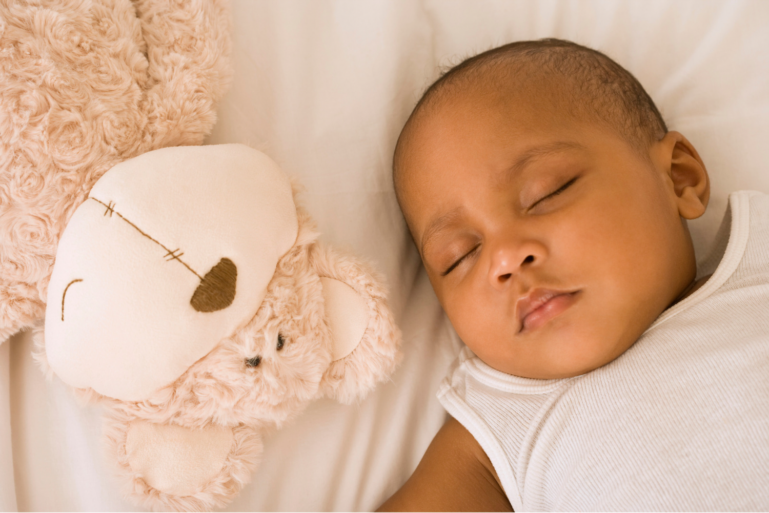 Baby sleeping with teddy bear in cot