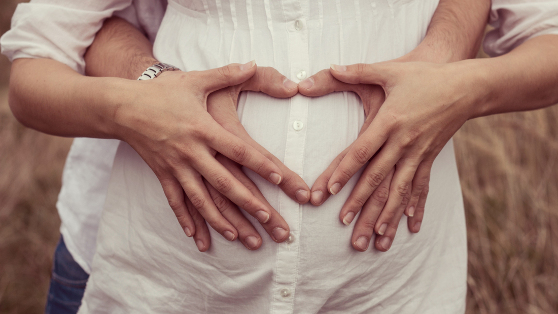 parents to be holding baby bump with heart shaped hands