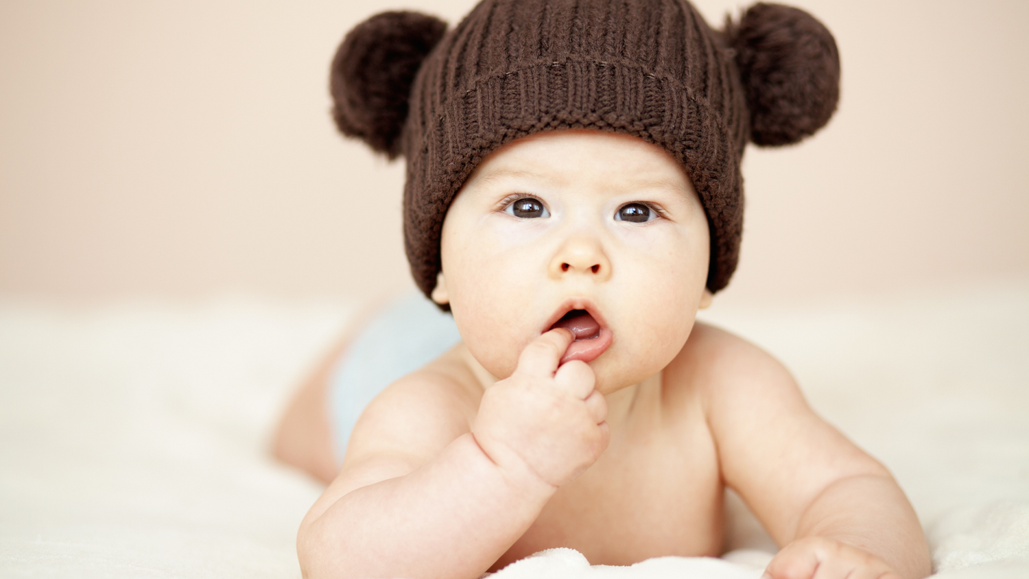 Baby in cute hat with hand in mouth 
